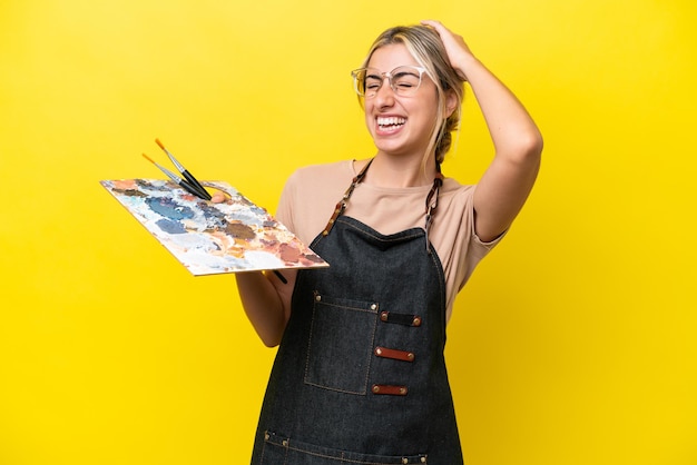 Young artist caucasian woman holding a palette isolated on yellow background smiling a lot