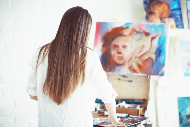 Foto giovane artista ragazza al lavoro in officina il pennello dipinge l'ispirazione della tela