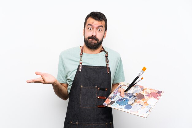 Young artist man holding a palette over having doubts while raising hands