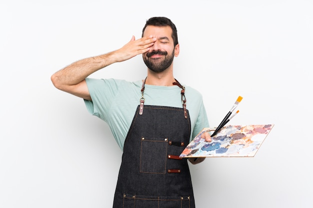 Young artist man holding a palette over isolated background covering eyes by hands