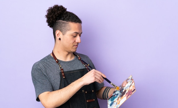 Young artist man holding a palette over isolated purple wall