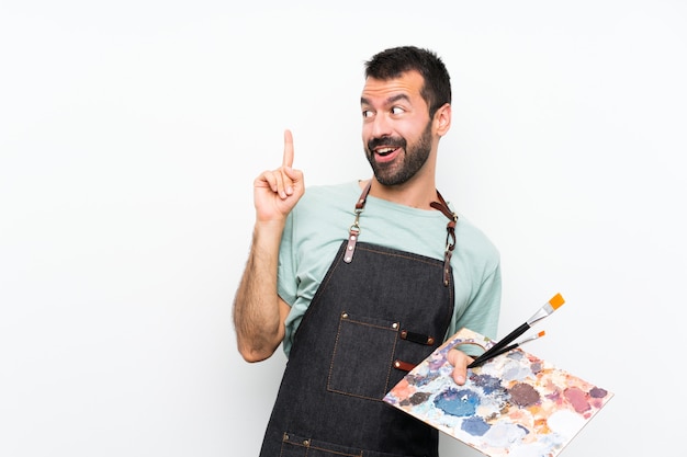 Young artist man holding a palette over isolated wall intending to realizes the solution while lifting a finger up