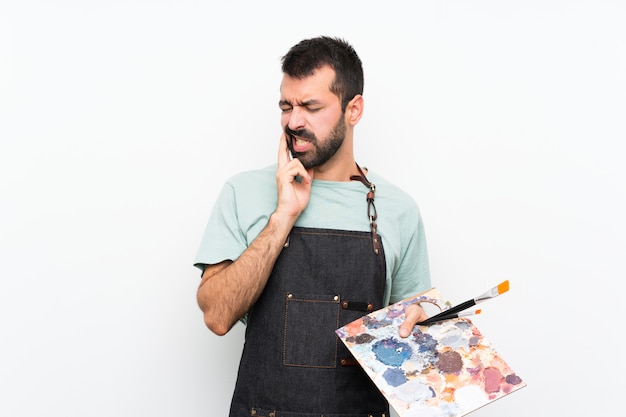 Young artist man holding a palette over isolated wall with toothache