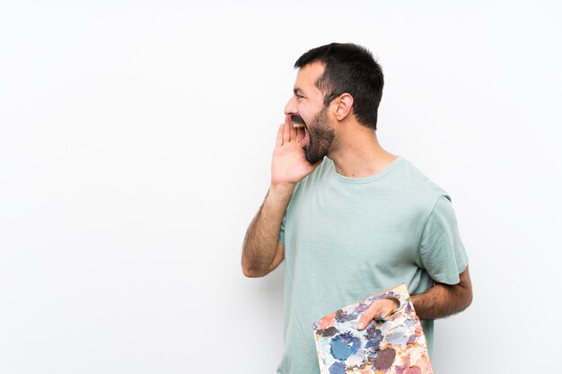 Young artist man holding a palette shouting