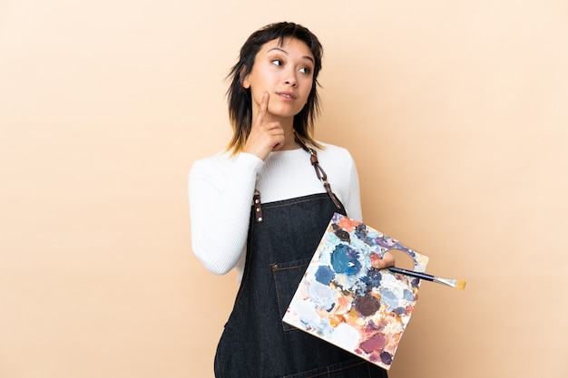 Photo young artist man holding a palette over wall thinking an idea