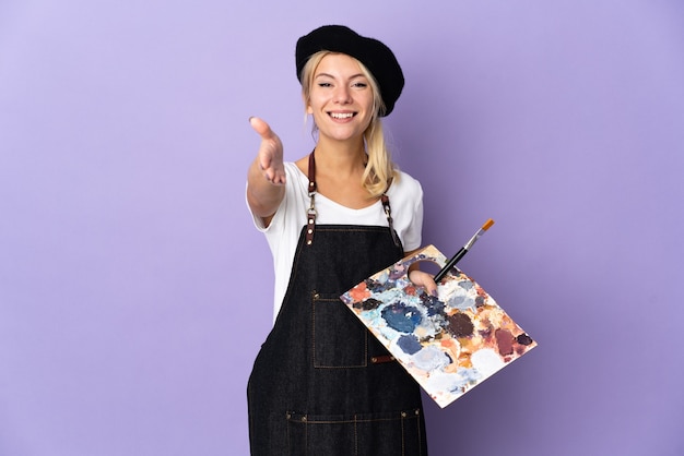 Young artist Russian woman holding a palette isolated on purple background shaking hands for closing a good deal