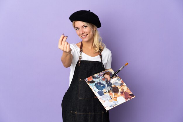 Photo young artist russian woman holding a palette isolated on purple making money gesture