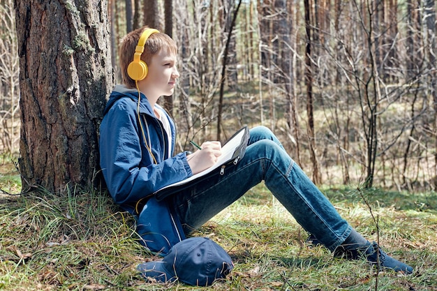 Young artist sits in pine forest and plein air painting and listens to music Sunny day creative leisure