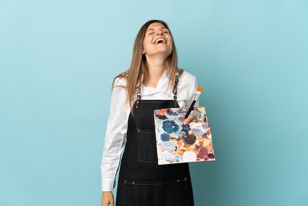 Young artist Slovak woman isolated on blue wall laughing