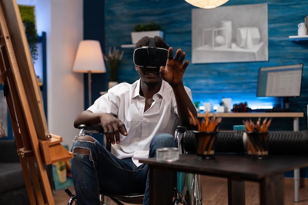 Young artist with virtual reality goggles imagining draw illustration while working at art masterpiece in creativity studio. Man with disability drawing sketch on canvas using graphic pencil