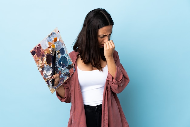 Young artist woman holding a palette over blue wall having doubts.