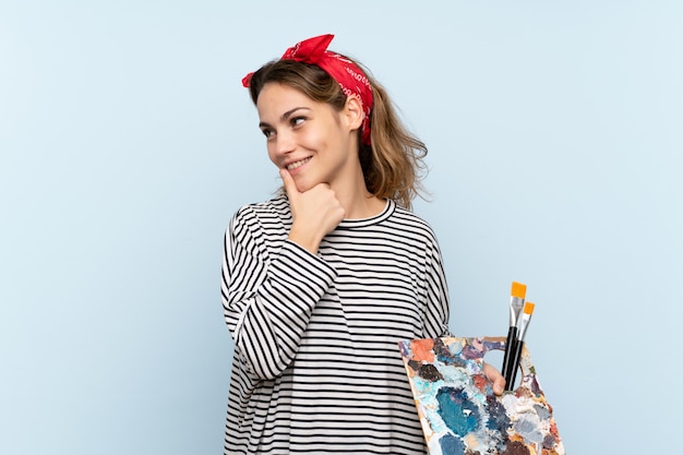 Photo young artist woman holding a palette over isolated blue thinking an idea and looking side