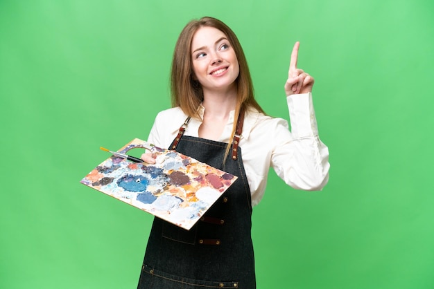 Young artist woman holding a palette over isolated chroma key background pointing up a great idea