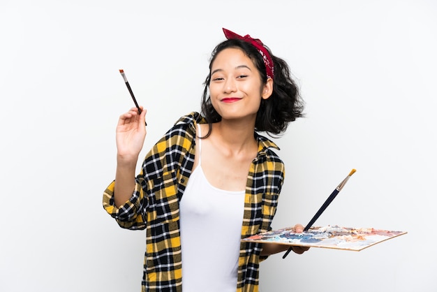 Молодой художник женщина держит палитру над изолированной белой стеной