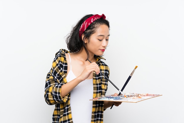 Young artist woman holding a palette over isolated white wall