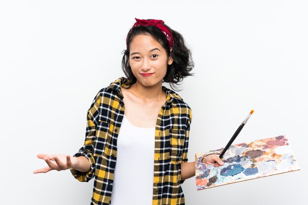 肩を持ち上げながら疑問ジェスチャーを作るパレットを保持している若いアーティストの女性