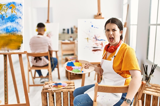 예술 스튜디오에서 캔버스에 그림을 그리는 젊은 예술가 여성 화가 분노와 공격적인 개념으로 좌절하고 분노한 소리를 지르며 화가 났습니다.