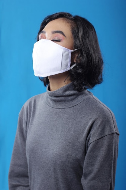 写真 医療用フェイスマスクを着用し、青の背景に目を閉じるアジアの若い女の子