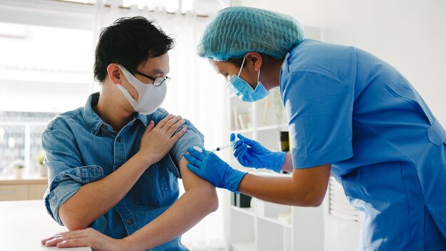 Photo young asia lady nurse giving covid19 or flu antivirus vaccine shot to senior male patient wear face mask protection from virus disease at health clinic or hospital office vaccination concept