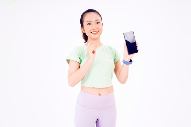 Young Asia lady show empty smart phone screen with positive expression smiles broadly dressed in casual clothing feeling happiness on blue background Mobile phone with white screen in female hand