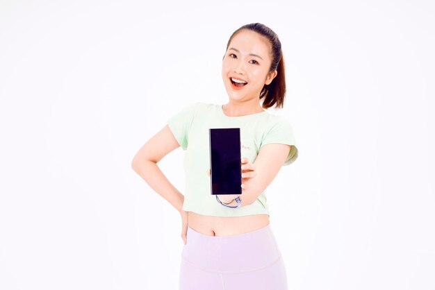 Young Asia lady show empty smart phone screen with positive expression smiles broadly dressed in casual clothing feeling happiness on blue background Mobile phone with white screen in female hand