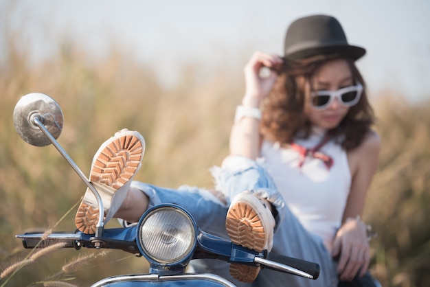 Young Asia woman is sitting on retro scooter outdoors at sunset time