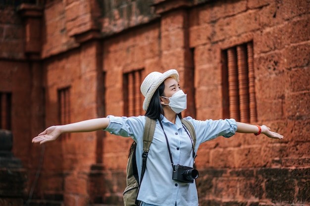 Foto giovane donna asiatica zaino in spalla che indossa cappello e maschera di protezione durante il viaggio in un sito storico