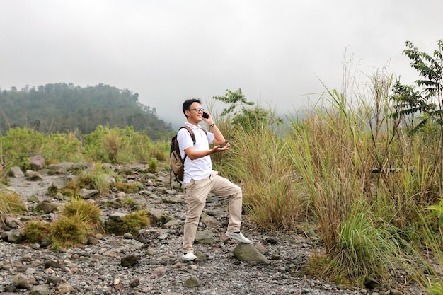 Young asian backpacker man is happy and smile when he looking smartphone when traveling in mountain