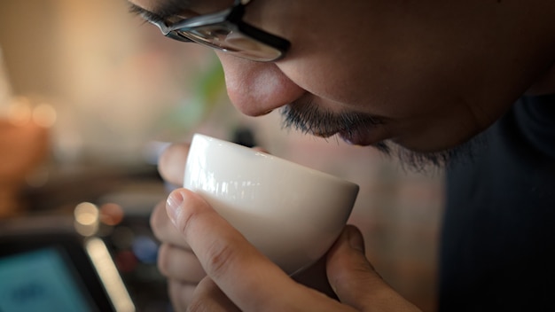 Photo young asian barista man holding ceramic cup close to his nose