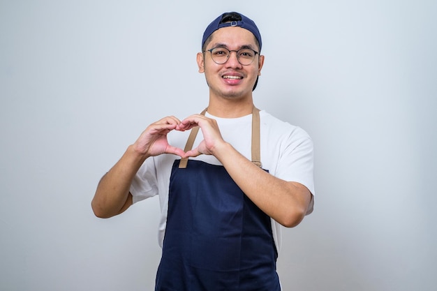 Giovane uomo asiatico del barista che fa il segno del cuore con le sue mani