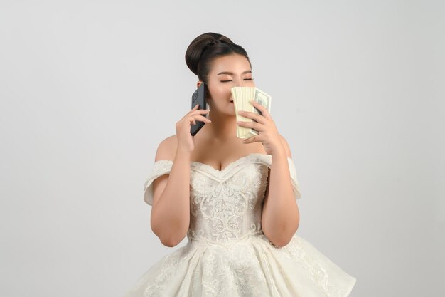 Young asian beautiful bride posting with smartphone and banknote in hand