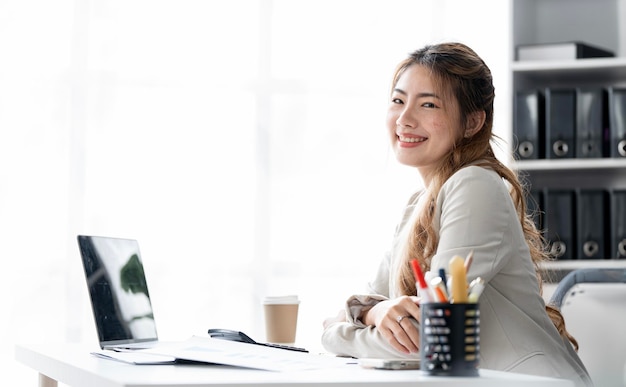 Young asian beautiful and charming businesswoman smiling and working on laptop computer at officex9