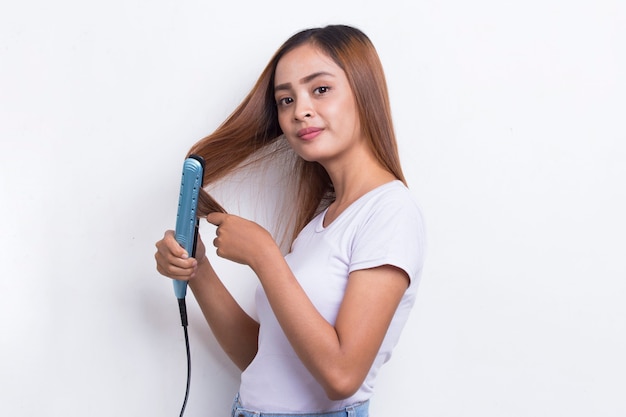 Young asian beautiful happy woman straightening hair with hair straightener on white background
