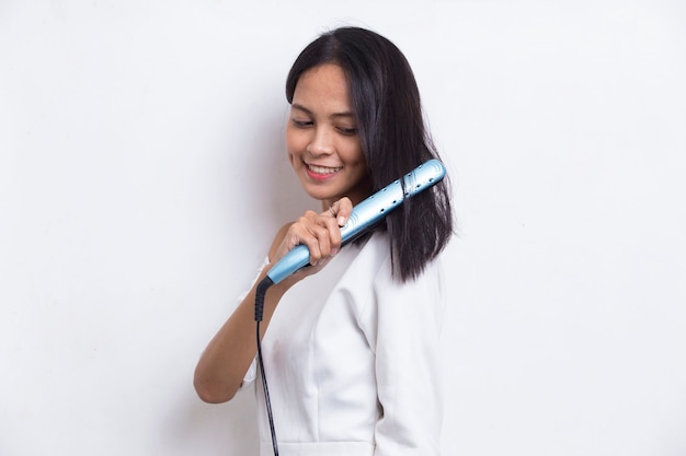 young asian beautiful happy woman straightening hair with hair straightener on white