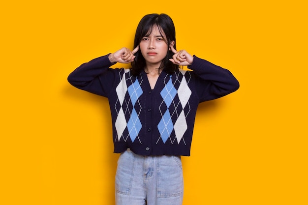 young asian beautiful woman covering both ears with hands isolated on yellow background