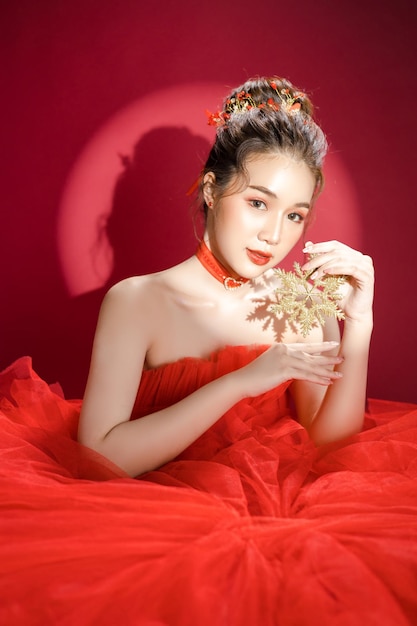 Young Asian beautiful woman model in a posh stylish luxury red dress on a red background isolated