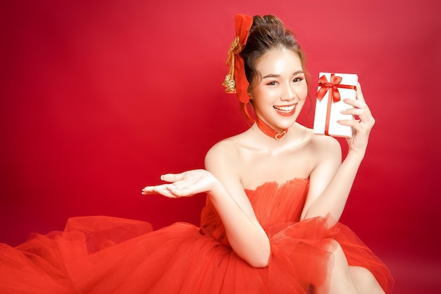 Модель молодой азиатской красивой женщины в шикарном стильном роскошном красном платье на красном фоне изолированы