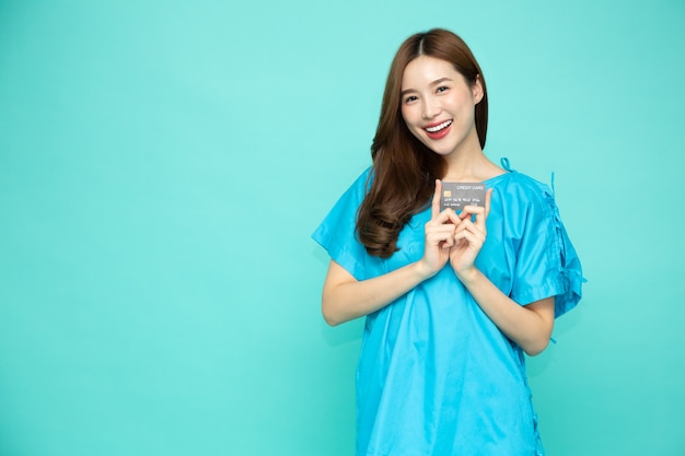 Молодая азиатская красивая женщина-пациент, держащая кредитную карту, изолированную на зеленом фоне