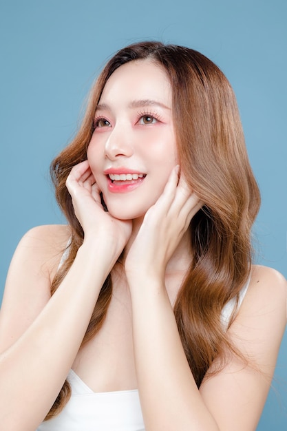 若いアジアの美しさの女性の顔に韓国のメイク スタイルと孤立した青い背景に完璧なきれいな肌を持つ巻き毛の長い髪 フェイシャル トリートメント美容形成外科