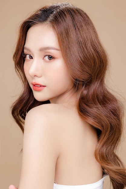 얼굴에 한국식 화장을 한 젊은 아시아 미녀 곱슬머리와 고립된 베이지색 배경의 완벽한 피부 페이셜 트리트먼트 코스메탈로지 성형 수술