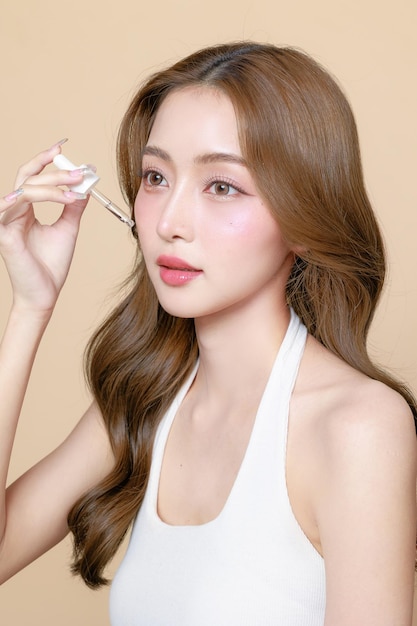 Young Asian beauty woman curly long hair with korean makeup style on face and using pipette to apply serum on skin on isolated beige background Facial treatment Cosmetology plastic surgery