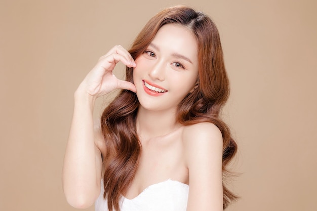 Young Asian beauty woman curly long hair with korean makeup style touch her face and perfect skin on isolated beige background Facial treatment Cosmetology plastic surgery