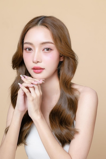 アジアの美人女性長で韓国のメイクアップスタイルで顔を触れベージュ色の背景に完璧な皮膚を触れます 顔の治療美容整形外科