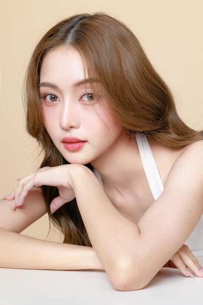 Young Asian beauty woman curly long hair with korean makeup style touch her face and perfect skin on isolated beige background Facial treatment Cosmetology plastic surgery