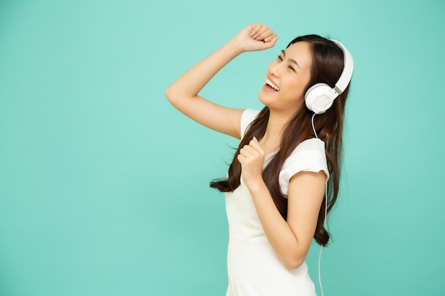 Young Asian beauty woman dancing and listening music with headphones in playlist song application on smartphone isolated on green wall