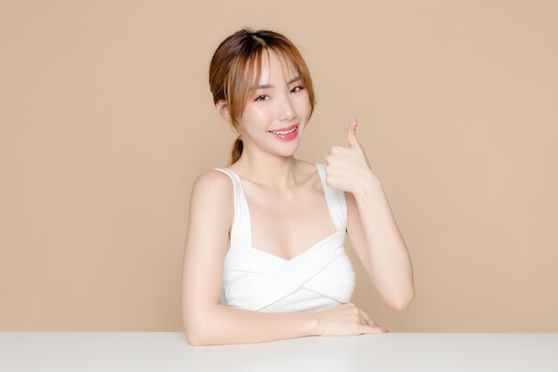 Young Asian beauty woman pony tail hair with korean makeup style on face and perfect skin show thumb up on isolated beige background Facial treatment Cosmetology Spa Aesthetic plastic surgery