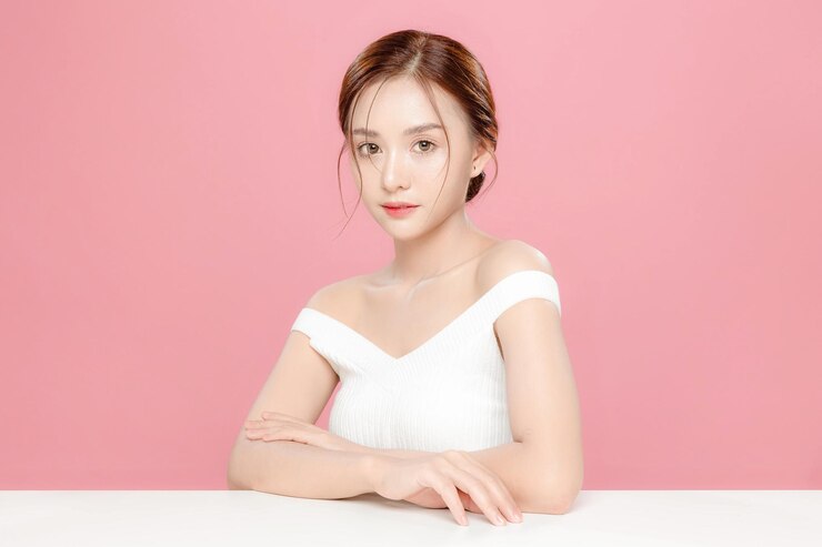 年轻的亚洲美女用韩国化<unk>风格拉回头发触摸她的脸和完美的皮肤在孤立的粉红色背景面部治疗美容整形手术