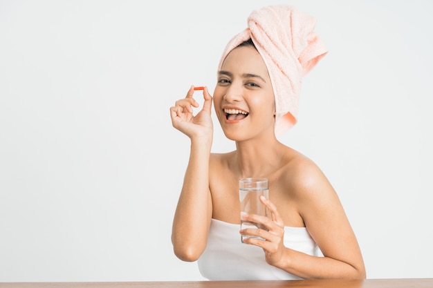 Young asian beauty young woman eating pills and drinking water on white wall.