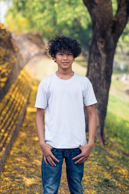 Young Asian boy smiling under a yellow Handroanthus chrysanthus tree in full bloom