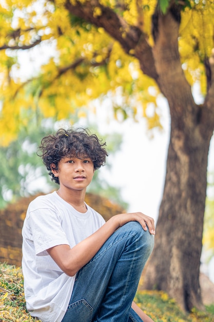 Young Asian boy smiling under a yellow Handroanthus chrysanthus tree in full bloom